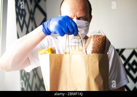 Lieferung Mann in Schutzmaske und medizinische Handschuhe liefert Essen zum Mitnehmen. Lieferung von Lebensmitteln während der Quarantäne. Covid-19-Konzept Stockfoto