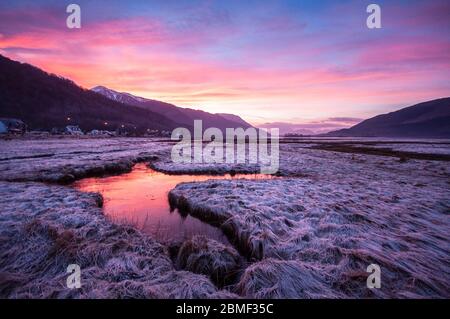 Der Sonnenuntergang wirft einen roten Himmel, der sich in gefrorenen Pools am Ufer des Loch Leven in Glen Coe im schottischen Hochland widerspiegelt. Stockfoto