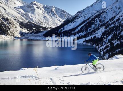 Radfahrer Fahrten auf Schnee Ufer des Bergsees in Almaty, Kasachstan Stockfoto