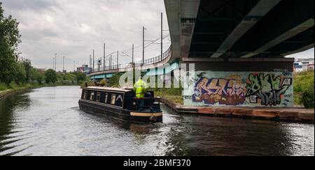 Manchester, England, UK - 21. Mai 2011: Ein Mann fährt ein traditionelles Schmalboot entlang des Bridgewater Kanals, unter einem modernen Viadukt der Metrolink Stockfoto