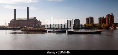 Ein Schlepper schlepper schlepper schlepper ein Schiff mit containerisiertem Abfall entlang der Themse vorbei an Loots Road Power Station, World's End Estate und anderen Gebäuden an der Chelsea Waterfront. Stockfoto