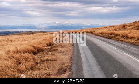 Schneebedeckte Berge des English Lake District erheben sich hinter Morecambe Bay, wie von Hare Appletree gesehen fiel in den Wald von Bowland Hügel. Stockfoto