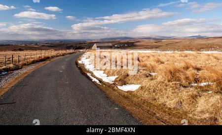 Eine schmale Landstraße windet sich durch raues Moorland auf den Hügeln des Forest of Bowland in Lancashire, mit den Hügeln der Yorkshire Dales darüber hinaus. Stockfoto