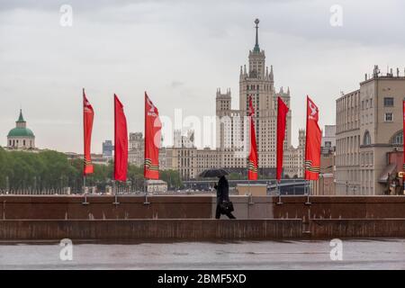 Moskau, Russland. 8. Mai 2020 die Bolschoi Moskvoretsky Brücke ist mit roten Bannern mit dem Bild des St. Georgs Band geschmückt, das dem 75. Jahrestag des Sieges über Nazi-Deutschland während des Zweiten Weltkriegs vor dem Hintergrund des berühmten Stalins Wolkenkratzers (Kotelnicheskaya-Ufergebäude) gewidmet ist. Im Zentrum von Moskau, Russland Stockfoto