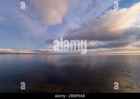 Tief fliegende weiße Wolken über der Wasseroberfläche eines großen Flusses bei Sonnenuntergang. Stockfoto