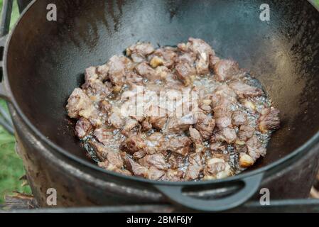 Pilaf Kochen in Kessel auf Feuer im Freien Serie. Die Stücke des Lammfleisches werden in kochendem Öl in der Pfanne auf Feuer gebraten. Schritt-für-Schritt-Prozess des Kochens pilaf. Stockfoto