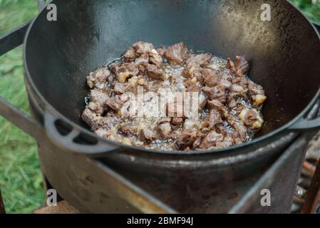 Pilaf Kochen in Kessel auf Feuer im Freien Serie. Die Stücke des Lammfleisches werden in kochendem Öl in der Pfanne auf Feuer gebraten. Schritt-für-Schritt-Prozess des Kochens pilaf. Stockfoto