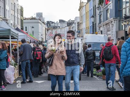 Junge Paare mit Kokosnuss mit Stroh und Telefon in der Hand genießen einander in Portobello Road. Marktstände, viktorianische Reihenhäuser, Händler mit Waren Stockfoto