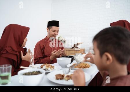 Muslimische Familie sitzen und beten, wenn sie zu Hause gemeinsam brechen Stockfoto