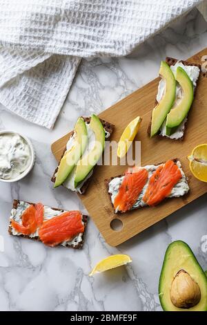 Frühstück am Morgen, zartes hausgemachtes Weichkäse auf Crackern mit geräucherter Forelle und Avocado Stockfoto