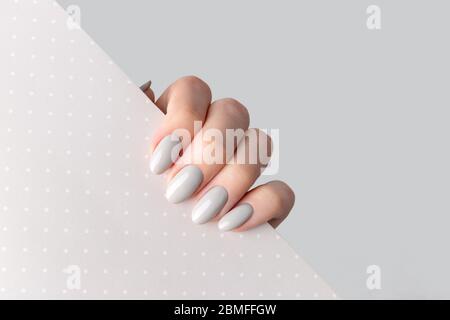 Schöne Womans Hand mit Maniküre Nahaufnahme auf Polka Punkt Hintergrund. Grauer Nagellack Stockfoto