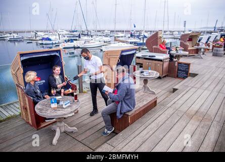 09. Mai 2020, Mecklenburg-Vorpommern, Kühlungsborn: Ein Kellner bringt die Menüs zur Familie Krause aus Rostock auf die Terrasse des Restaurants Vielmeer. Die Restaurants in Mecklenburg-Vorpommern können aufgrund der Corona-Schutzmaßnahmen wieder unter strengen Hygienebedingungen und weniger Sitzplätzen bedient werden. Seit mehreren Wochen waren Restaurants in ganz Deutschland wegen des Corona-Virus geschlossen. Foto: Jens Büttner/dpa-Zentralbild/dpa Stockfoto