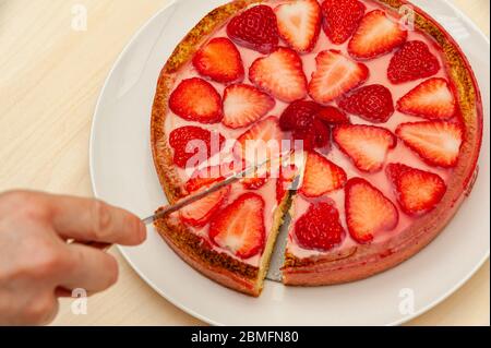 Hand schneiden köstliche hausgemachte Erdbeertart. Isoliert auf Holzhintergrund. Draufsicht. Nahaufnahme. Horizontale Aufnahme. Stockfoto