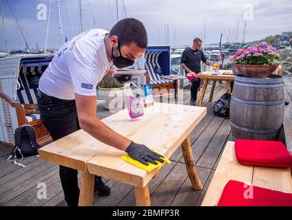 09. Mai 2020, Mecklenburg-Vorpommern, Kühlungsborn: Ein Kellner mit Gesichtsmaske und Handschuhen reinigt einen Gästetisch auf der Terrasse des wiedereröffneten Restaurants Vielmeer. Die Restaurants in Mecklenburg-Vorpommern können aufgrund der Corona-Schutzmaßnahmen wieder unter strengen Hygienebedingungen und weniger Sitzplätzen bedient werden. Mehrere Wochen waren Restaurants in ganz Deutschland wegen des Corona-Virus geschlossen. Foto: Jens Büttner/dpa-Zentralbild/dpa Stockfoto