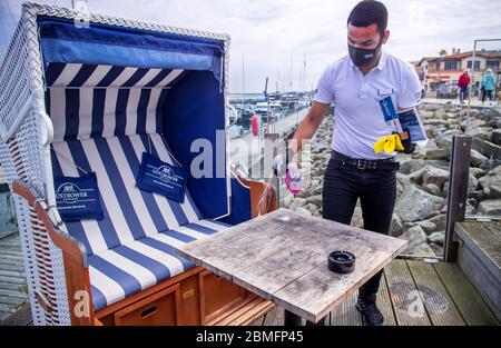 09. Mai 2020, Mecklenburg-Vorpommern, Kühlungsborn: Ein Kellner mit Gesichtsmaske und Handschuhen reinigt einen Gästetisch auf der Terrasse des wiedereröffneten Restaurants Vielmeer. Die Restaurants in Mecklenburg-Vorpommern können aufgrund der Corona-Schutzmaßnahmen wieder unter strengen Hygienebedingungen und weniger Sitzplätzen bedient werden. Mehrere Wochen waren Restaurants in ganz Deutschland wegen des Corona-Virus geschlossen. Foto: Jens Büttner/dpa-Zentralbild/dpa Stockfoto