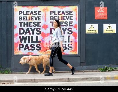 Glasgow, Schottland 9. Mai 2020 Junge Frau, die einen Hund an einem Plakat vorbeiläuft. Mit Prime Minster Boris Johnson, der am Sonntagabend eine Ankündigung auf dem Weg aus der Sperrung machen soll, passen sich die Menschen der neuen Normalität an. Quelle: Chris McNulty/Alamy Live News Stockfoto