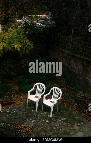 AJAXNETPHOTO. DEZEMBER 2005. WORTHING, WEST SUSSEX, ENGLAND. - SEITE AN SEITE - WEISSE PLASTIKGARTENSTÜHLE IN EINEM STÄDTISCHEN WOHNGEBÄUDE HINTERHOF HERBSTEINSTELLUNG FOTO:JONATHAN EASTLAND/AJAX REF:R50512 889 Stockfoto