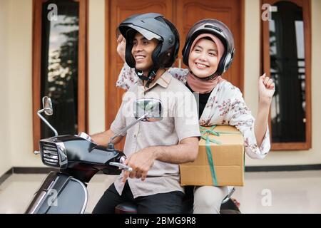 Fröhlicher muslim, der mit dem Motorroller auf eid mubarak mit Koffer unterwegs ist Stockfoto