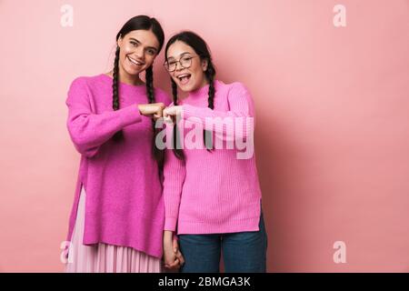 Bild von zwei jungen Mädchen im Teenageralter mit Zöpfen lächelnd und stoßen ihre Fäuste zusammen isoliert über rosa Hintergrund Stockfoto