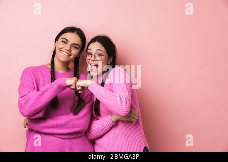 Bild von zwei jungen Mädchen im Teenageralter mit Zöpfen lächelnd und stoßen ihre Fäuste zusammen isoliert über rosa Hintergrund Stockfoto