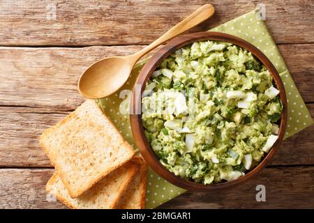 Sommer hausgemachten Salat von reifen Avocado mit gekochten Eiern und grünen Zwiebeln gewürzt mit Joghurt Nahaufnahme in einer Schüssel auf dem Tisch. Horizontale Ansicht von oben Stockfoto