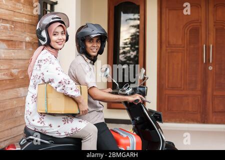 Fröhlicher muslim, der mit dem Motorroller auf eid mubarak mit Koffer unterwegs ist Stockfoto