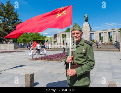 Mann in Uniform des Zweiten Weltkriegs und mit sowjetischer Flagge steht vor dem sowjetischen Kriegsdenkmal in Tiergarten, Berlin, um den 75. Jahrestag des Sieges über Nazi-Deutschland zu begehen Stockfoto
