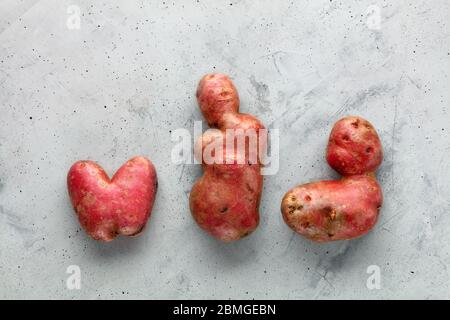 Hässliche Kartoffel in Form eines Herzens und Buchstaben auf einem Hintergrund aus grauem Beton. Stockfoto