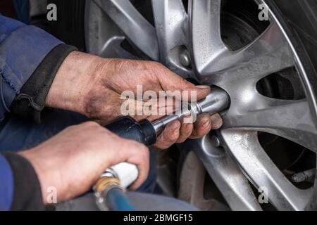 Mechaniker ohne Handschuhe ist das Rad auf Auto mit pneumatischen Schraubenschlüssel oder Hinterhof Mechaniker Schlagschrauber wechseln. Nahaufnahme Stockfoto