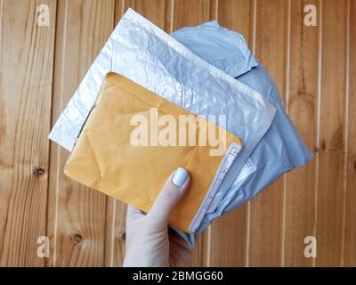 Drei Postpakete kleine Packung weiß, grau und gelb lagen auf Holzhintergrund Oberfläche in Frau Hand Stockfoto