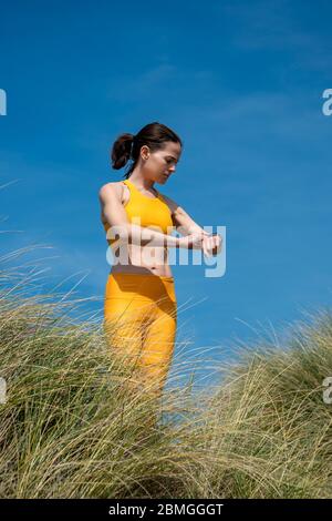 Eine sportliche Frau, die ihre Trainingsziele auf einer Smart Watch überprüft. Outdoor tragen gelbe Sportbekleidung. Stockfoto