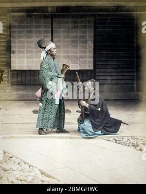 [ 1870er Japan - Kniender Samurai ] - EIN Samurai, der ein Schwert hält, kniet für eine Person, die ein Beamter zu sein scheint. Vintage Albumin-Fotografie aus dem 19. Jahrhundert. Stockfoto