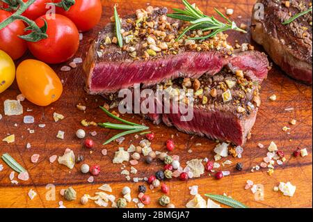 Saftiges, gegrilltes schwarzes, angus gereiftetes Steak mit Pistazien und gehackten Haselnüssen, Kirschtomaten, Rosmarin, Rosa- und Zitronensalz und Pfeffer in Körnern Stockfoto