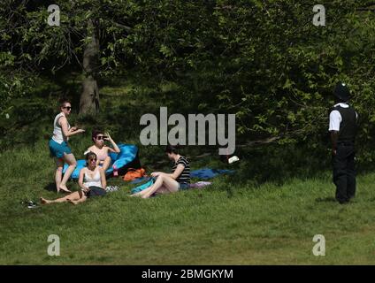 Ein Polizist zieht Sonnenanbeter in Greenwich Park, London, um die Ausbreitung des Coronavirus zu verhindern, während Großbritannien weiterhin gesperrt wird. Stockfoto