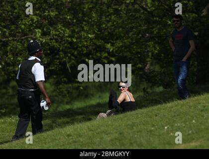 Ein Polizist zieht Sonnenanbeter in Greenwich Park, London, um die Ausbreitung des Coronavirus zu verhindern, während Großbritannien weiterhin gesperrt wird. Stockfoto