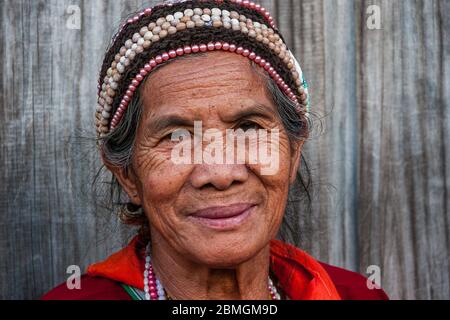 Banaue, Philippinen - Februar 2012: Ältere Frau in traditioneller Kleidung vor einer Holzwand Stockfoto