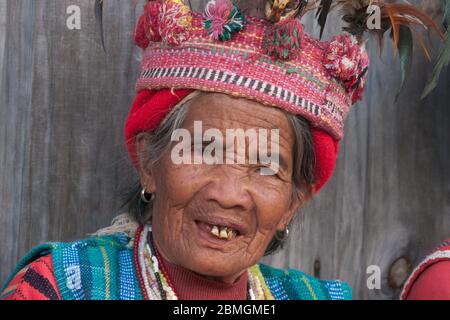 Banaue, Philippinen - Februar 2012: Ältere Frau in traditioneller Kleidung vor einer Holzwand Stockfoto