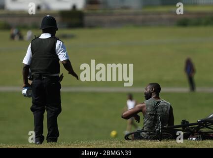 Ein Polizist zieht Sonnenanbeter in Greenwich Park, London, um die Ausbreitung des Coronavirus zu verhindern, während Großbritannien weiterhin gesperrt wird. Stockfoto