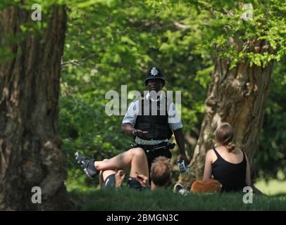 Ein Polizist zieht Sonnenanbeter in Greenwich Park, London, um die Ausbreitung des Coronavirus zu verhindern, während Großbritannien weiterhin gesperrt wird. Stockfoto