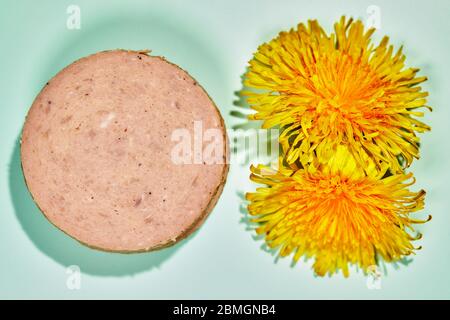 Dänische Fleischwurst ('frikadellepølse'), in Scheiben geschnitten, mit Löwenzahn-Blüten Stockfoto