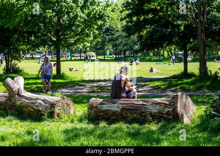 9. Mai 2020, London, Großbritannien - Mann, der auf das Mobiltelefon im Mile End Park schaut an einem Wochenende im heißen Frühling während des Ausbruchs der Coronavirus-Pandemie sonnen sich die Menschen trotz der Einschränkungen der staatlichen Lockdown im Park Stockfoto