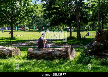 9. Mai 2020, London, Großbritannien - Mann, der auf das Mobiltelefon im Mile End Park schaut an einem Wochenende im heißen Frühling während des Ausbruchs der Coronavirus-Pandemie sonnen sich die Menschen trotz der Einschränkungen der staatlichen Lockdown im Park Stockfoto