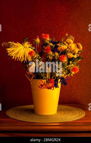 Welkende Blumen einschließlich Mütter, Chrysanthemen, Nelken in gelben Eimer Stockfoto