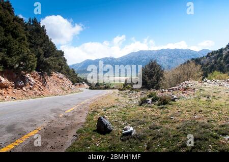 Eine einsame, einsame Straße führt durch die Berge oder das Hochland auf der griechischen Insel Kreta. Die Straße verliert sich am Horizont. Weiße Wolken können b Stockfoto