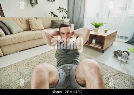 Junge aktive schweißtreibende Sportler, die während der Quarantäne zu Hause sitzen, vor der Kamera auf dem Teppich im Wohnzimmer sitzen Stockfoto