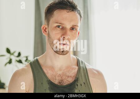 Junge schweißtreibende Sportler in Weste vor der Kamera in häuslicher Umgebung nach hartem Training am Morgen auf Quarantäne stehen Stockfoto