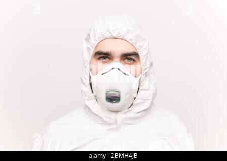 Kopf eines jungen Mannes mit blauen Augen, der Atemschutzmaske und weiße Schutzhüllen trägt, die isoliert vor der Kamera stehen Stockfoto