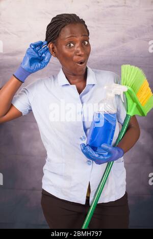 Junge Putzfrau, die der Neuheit zuhört, trägt Handschuhe und hält eine Bürste und eine Flasche Reinigungsmittel in der Hand Stockfoto