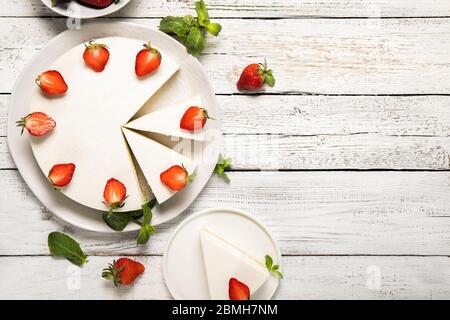 Teller mit leckerem Käsekuchen mit Erdbeeren und Minze auf Holzuntergrund. Blick von oben Stockfoto