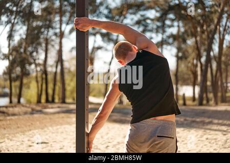 Unkenntlich kaukasischen Männer Outdoor-Training Cross-Training Morgen Training Rücken Ansicht Stretching Arm vor dem Training Sportplatz Natur Wald Hea Stockfoto